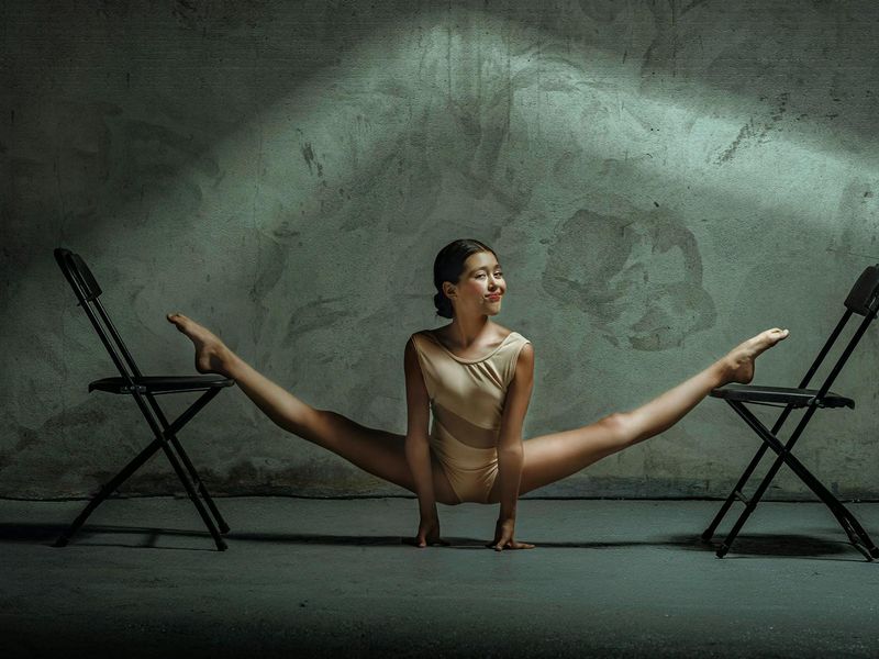A person performing a slow, controlled leg stretch in a spacious, sunlit studio.